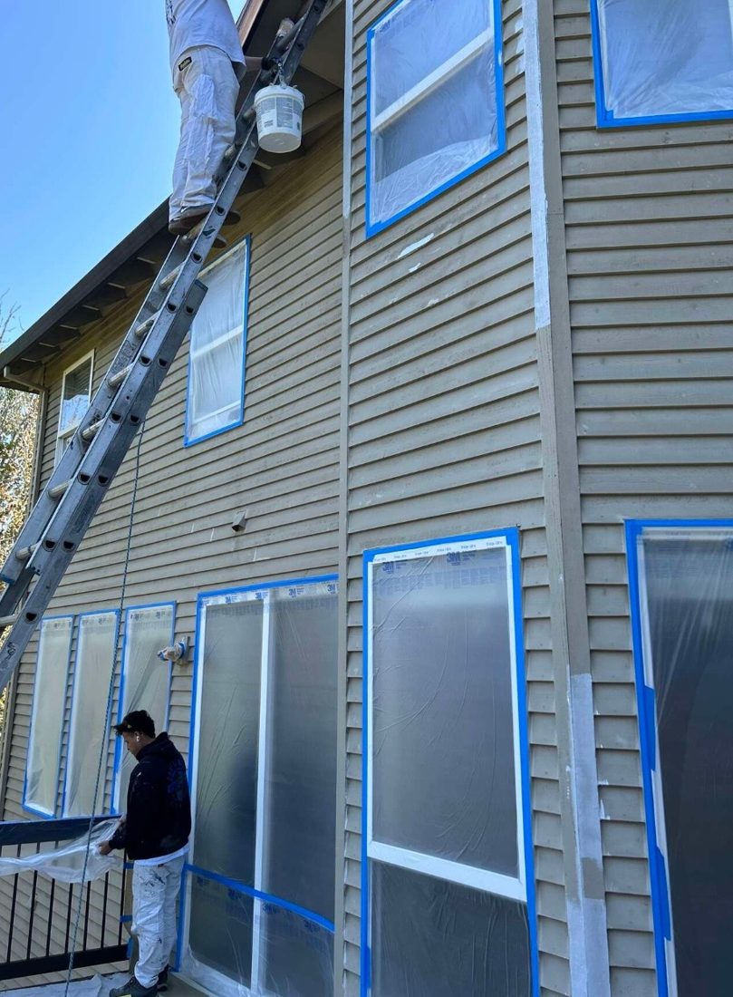 Crew masking windows and prepping siding before exterior painting
