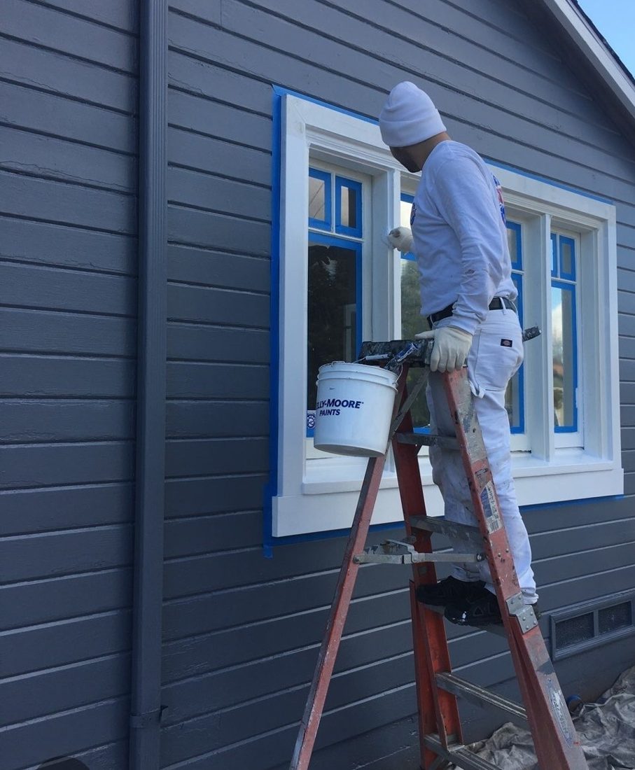 Painter cutting in white window trim against fresh gray siding